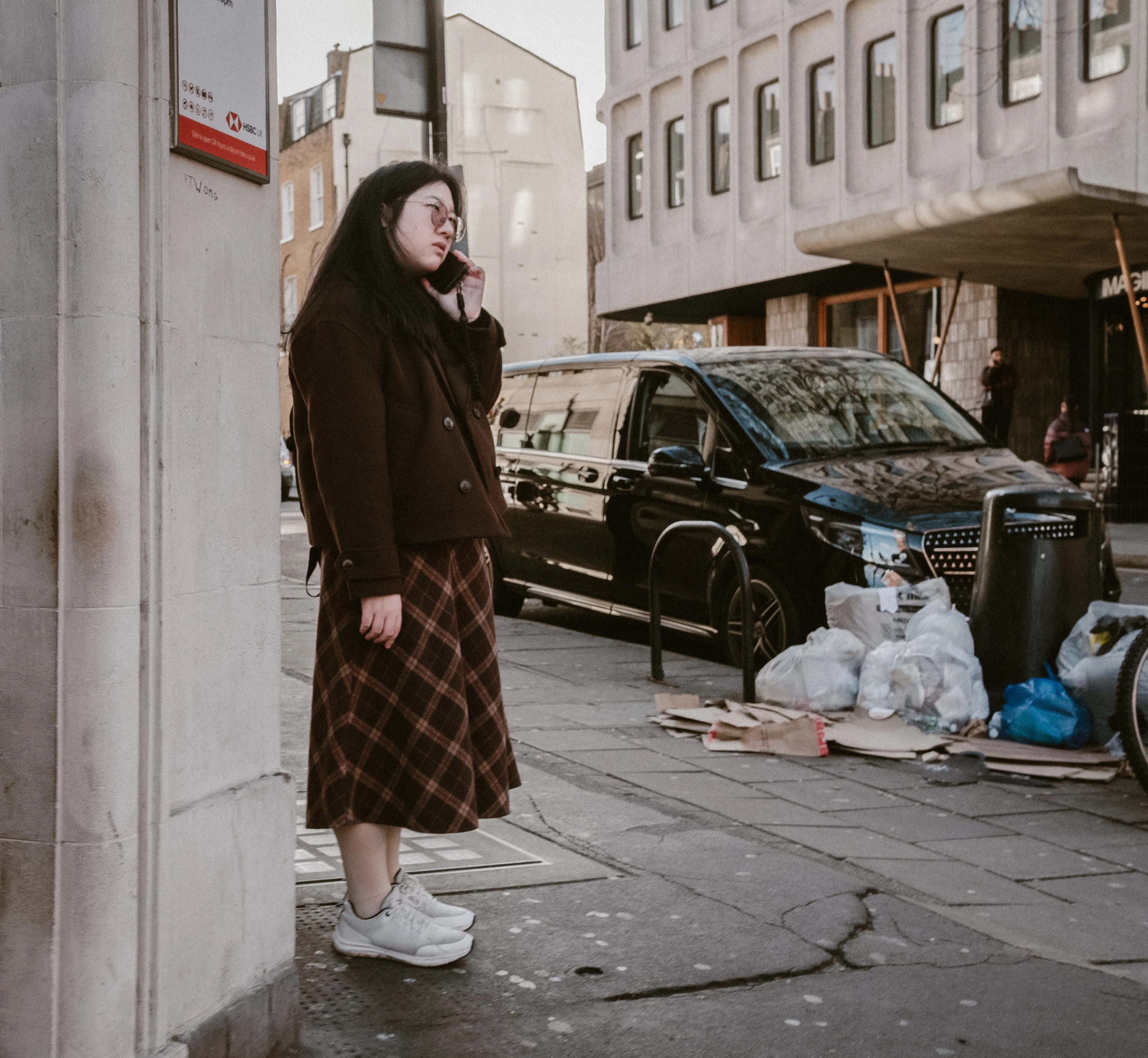 Woman in a dark coat beside a doorway on a city pavement