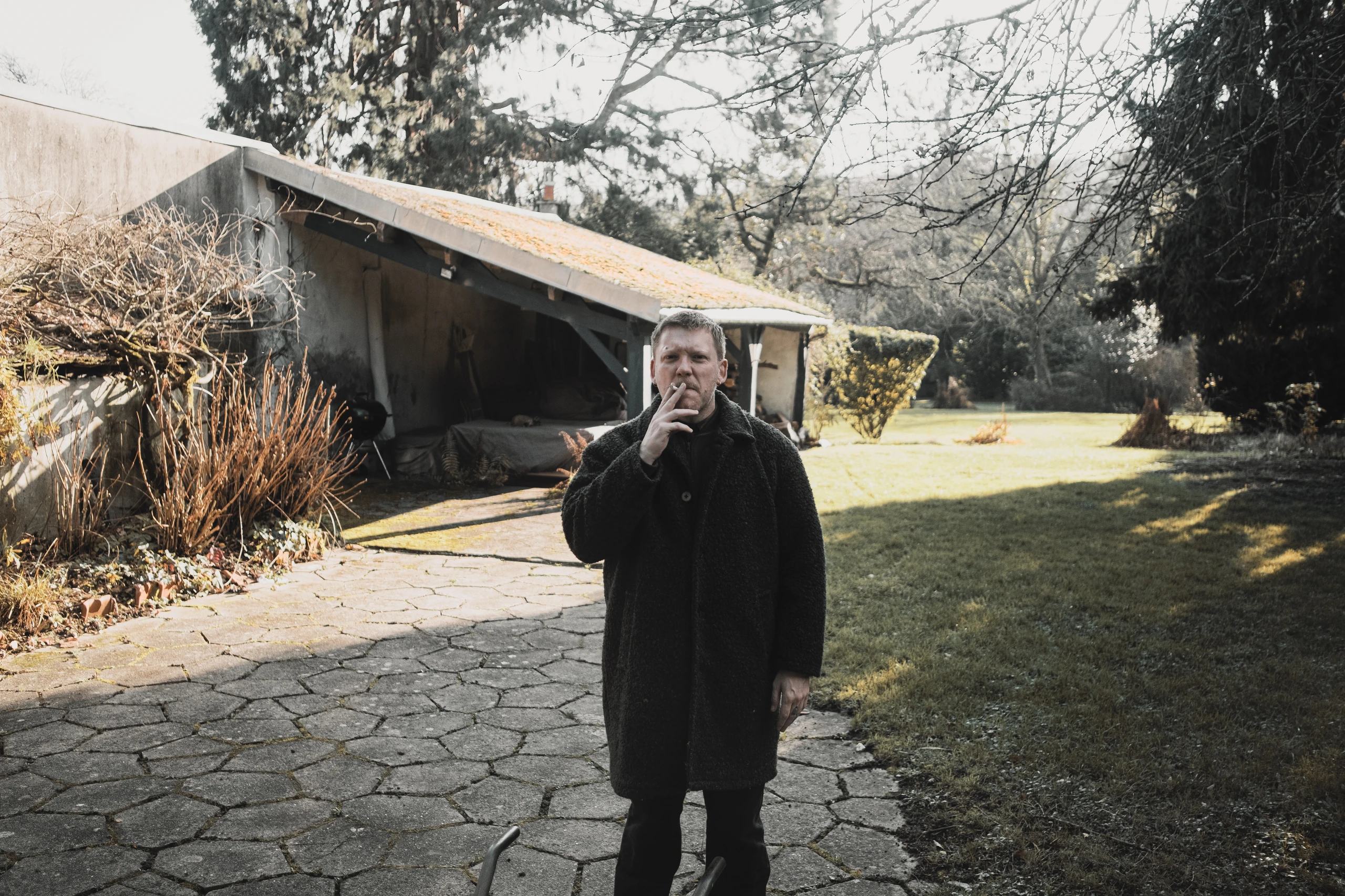 Man smoking beside a garden shed in winter sunlight