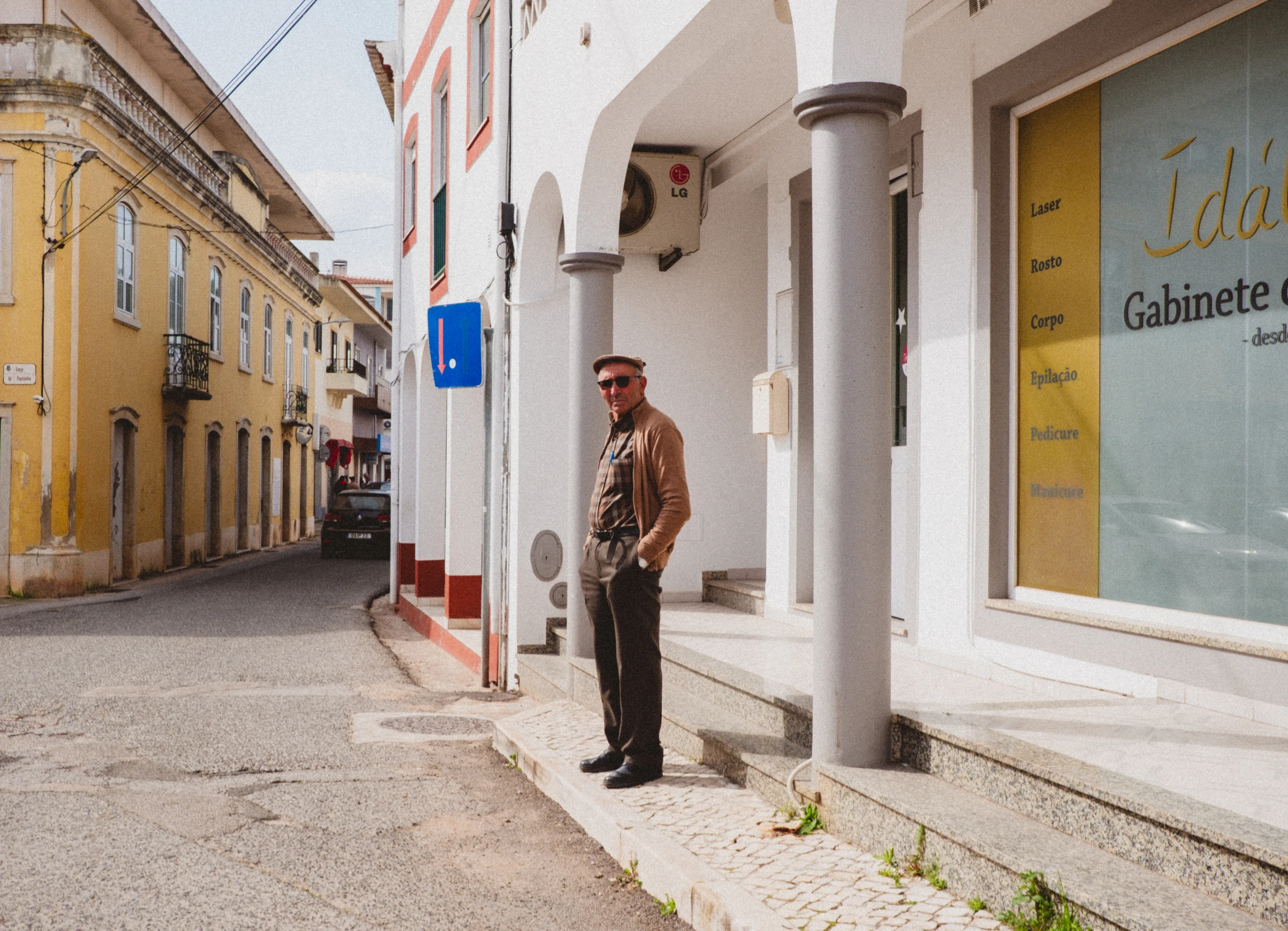 Man in sunglasses standing beneath white arches on a sunlit street