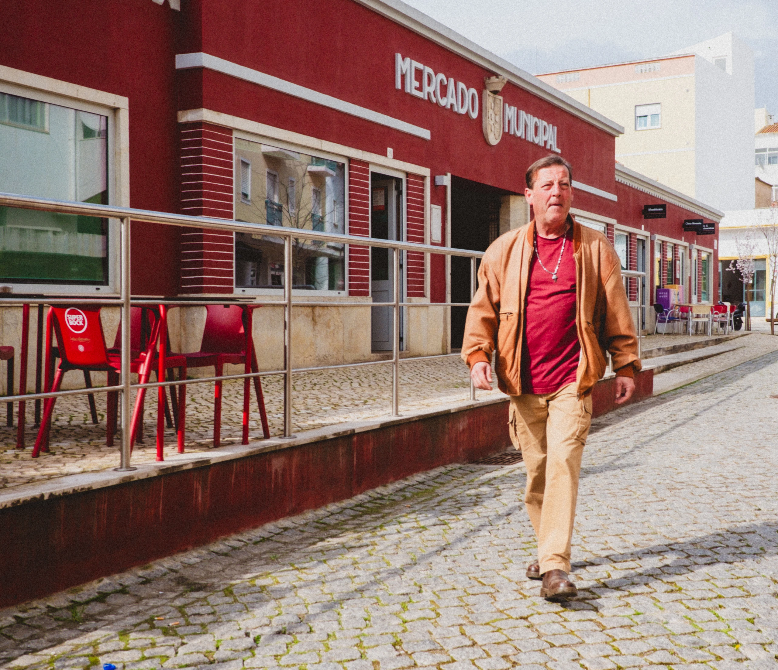 Man in tan clothing walking past a red market building