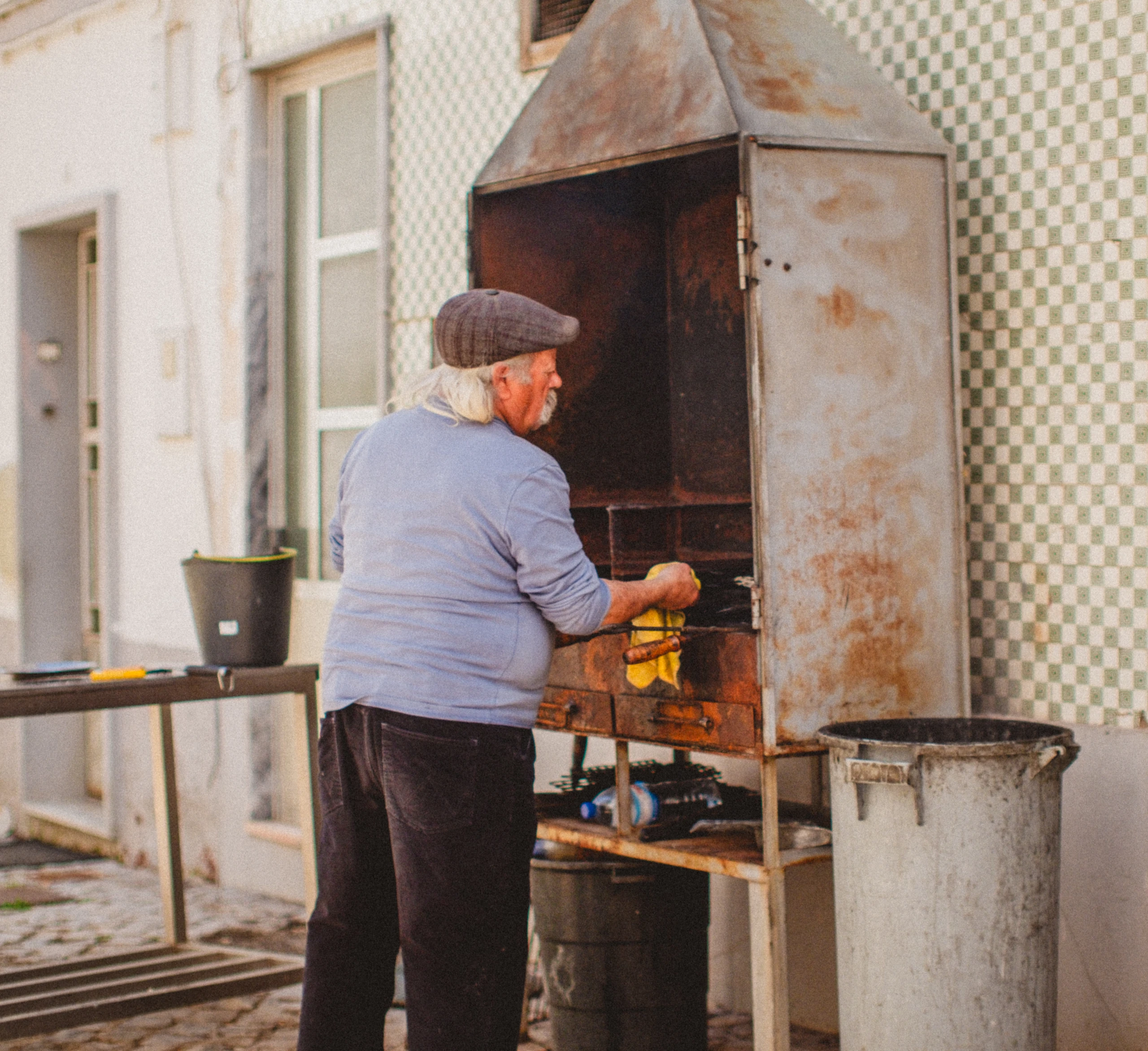 Man in a flat cap cooking at a tall outdoor grill