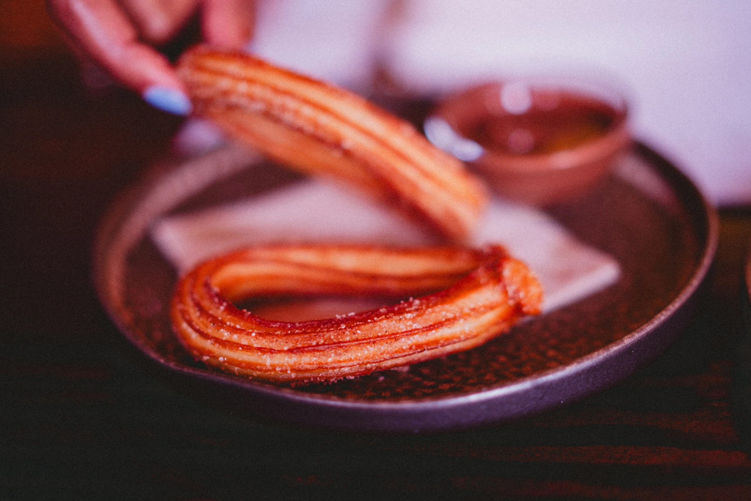 Hand lifting a churro above a plate and cup of chocolate