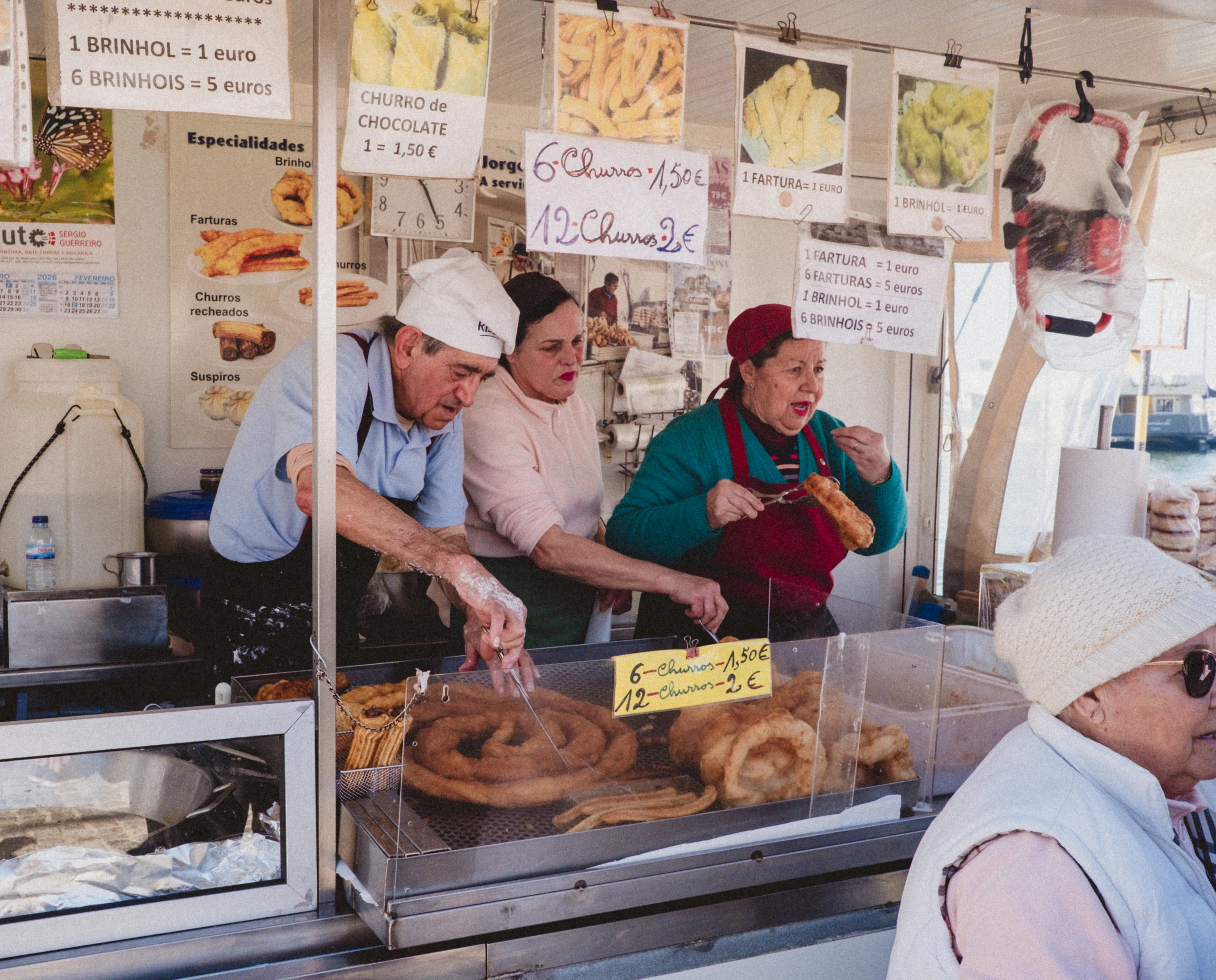 Three people preparing and serving churros behind a busy market counter