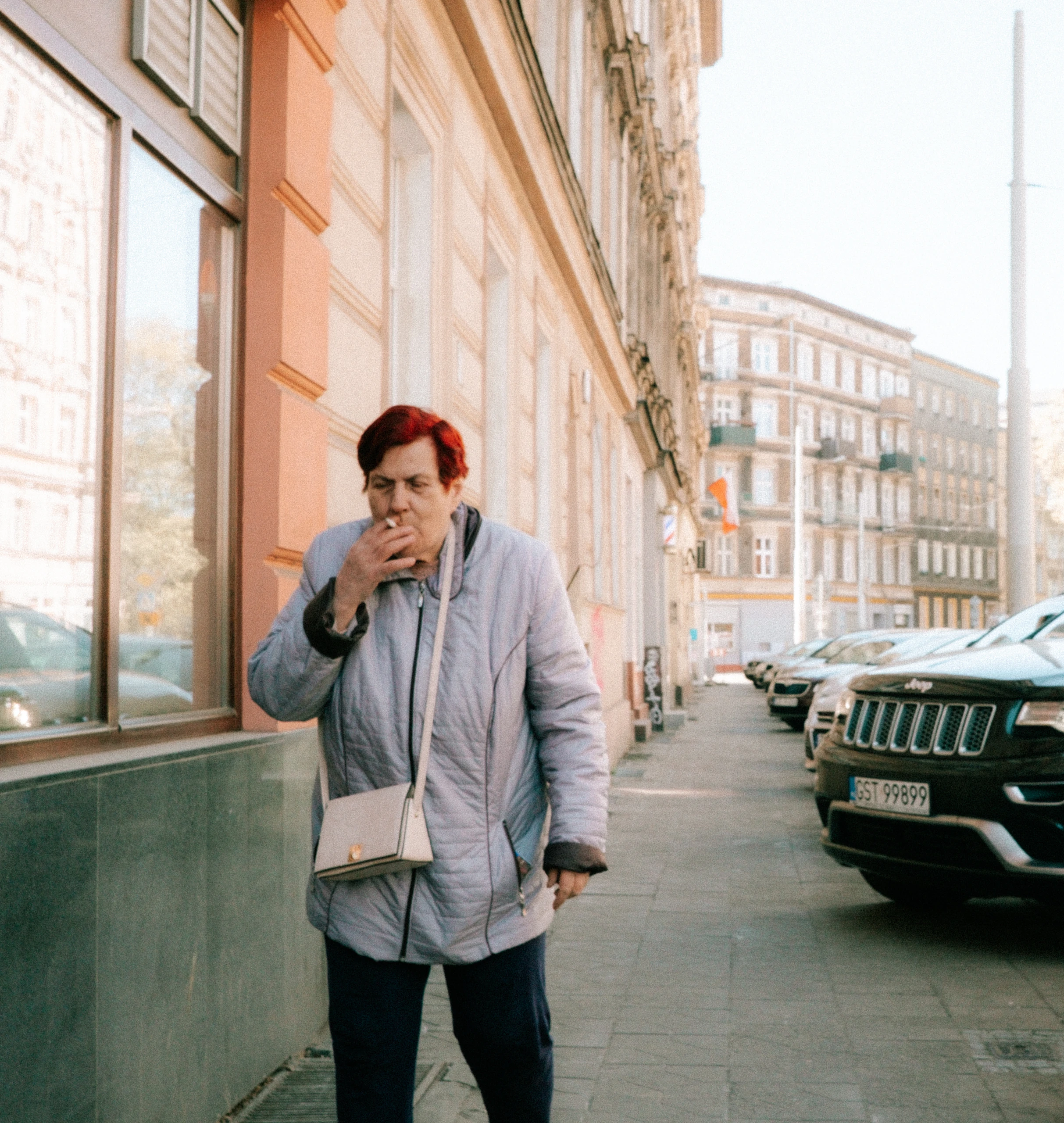 Woman in a light blue jacket smoking on a city pavement