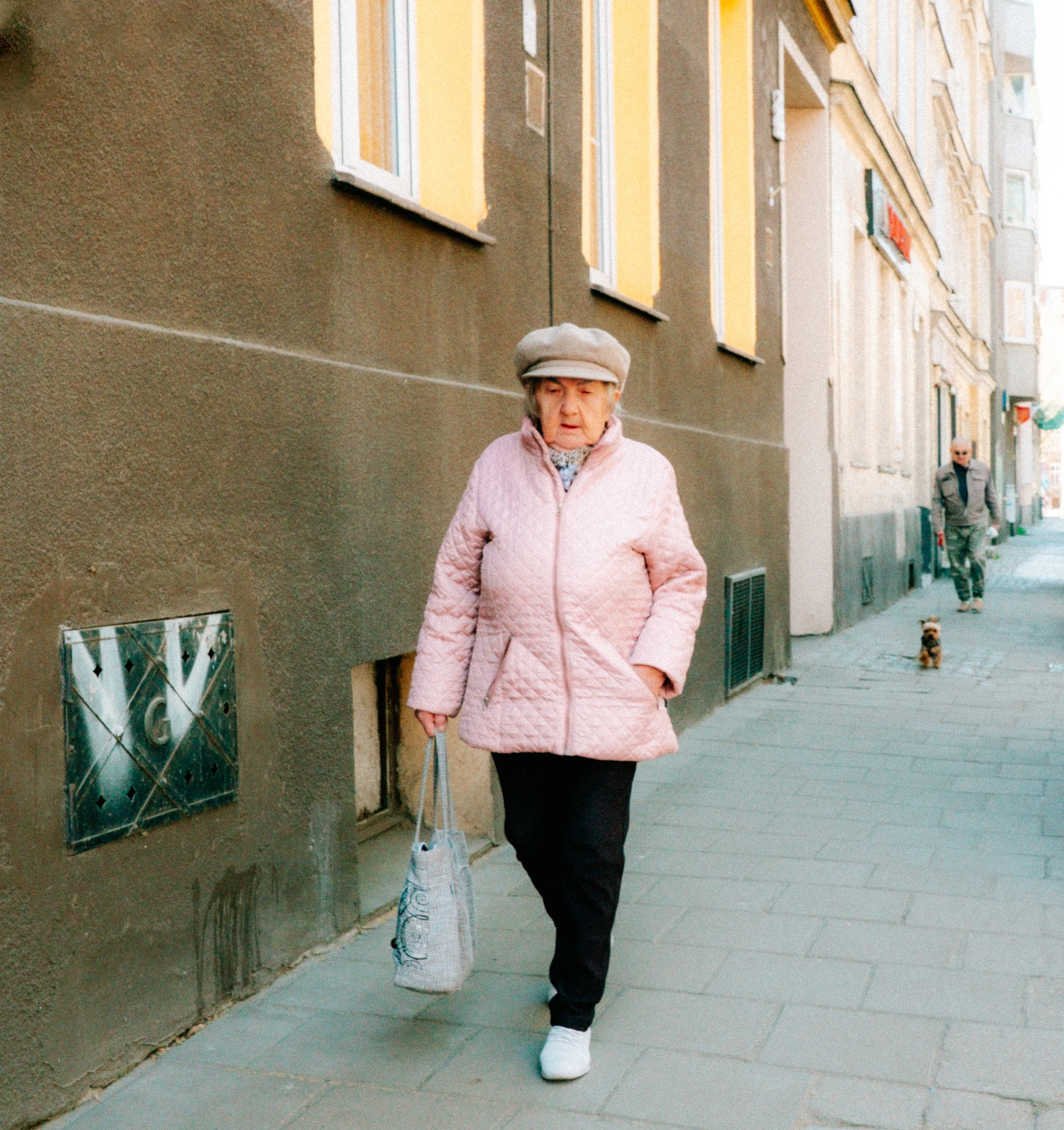 Woman in a pink jacket and grey cap walking along a city pavement