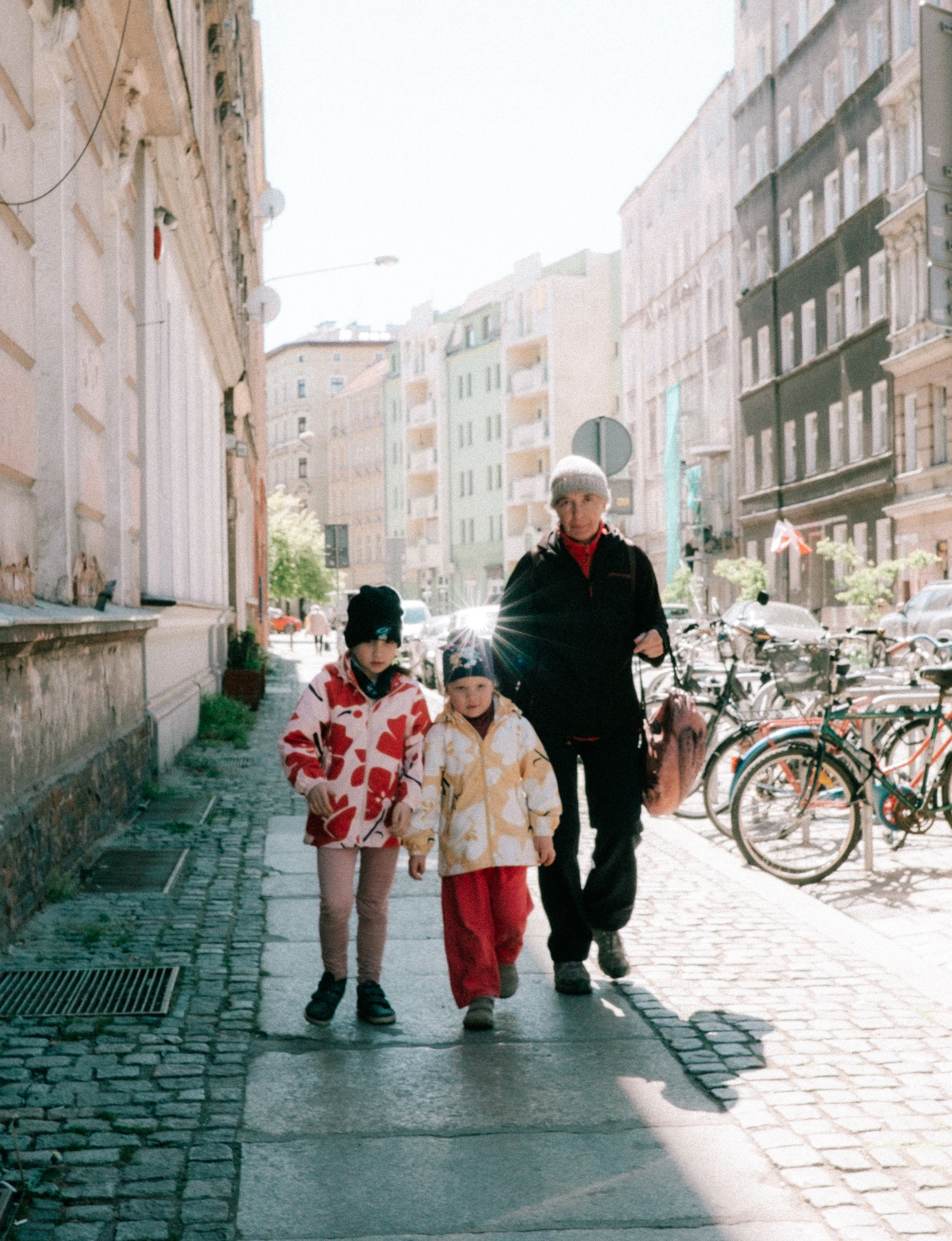 Older man and two children walking along a sunny city pavement