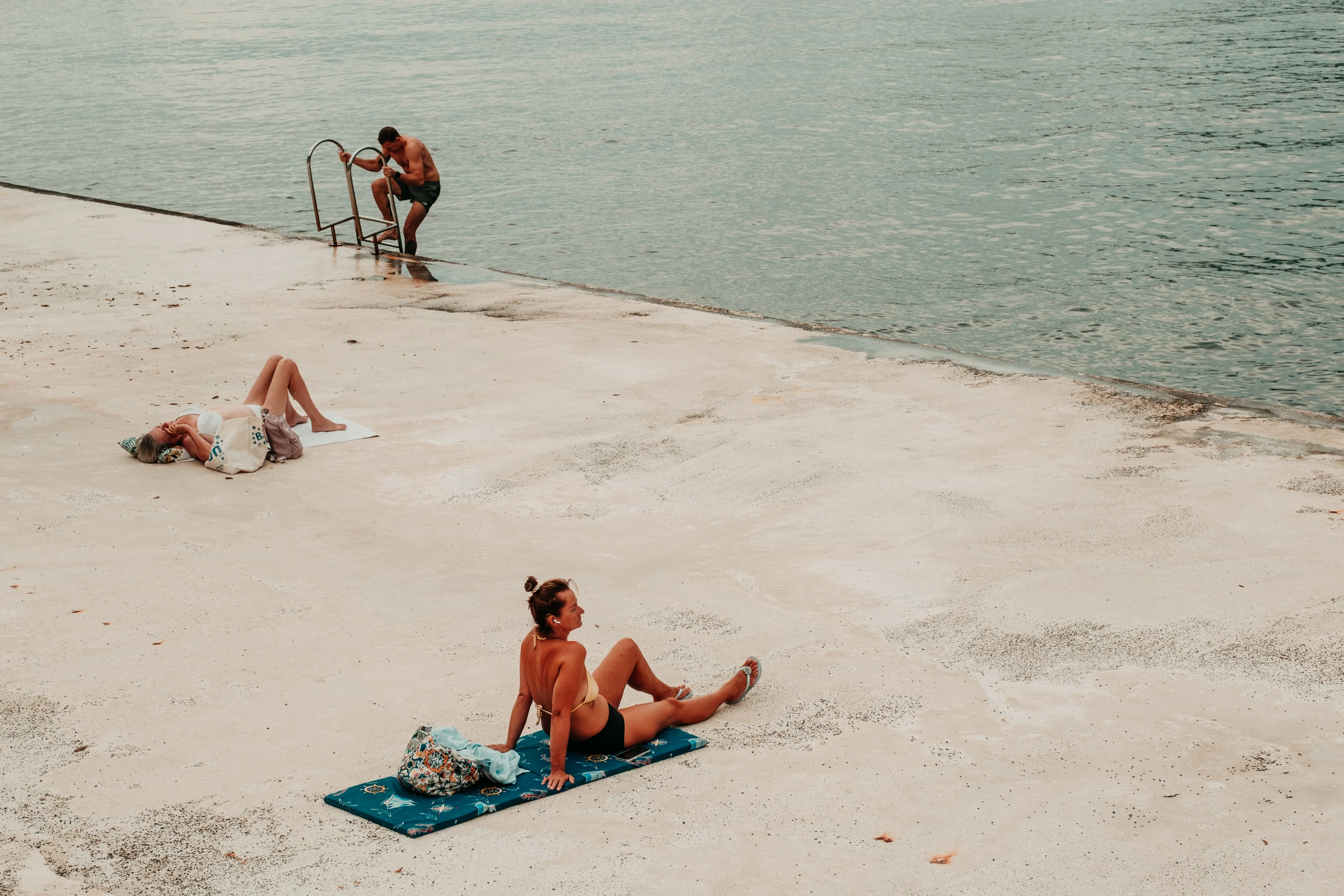 People sunbathing on a pale concrete waterfront beside calm water
