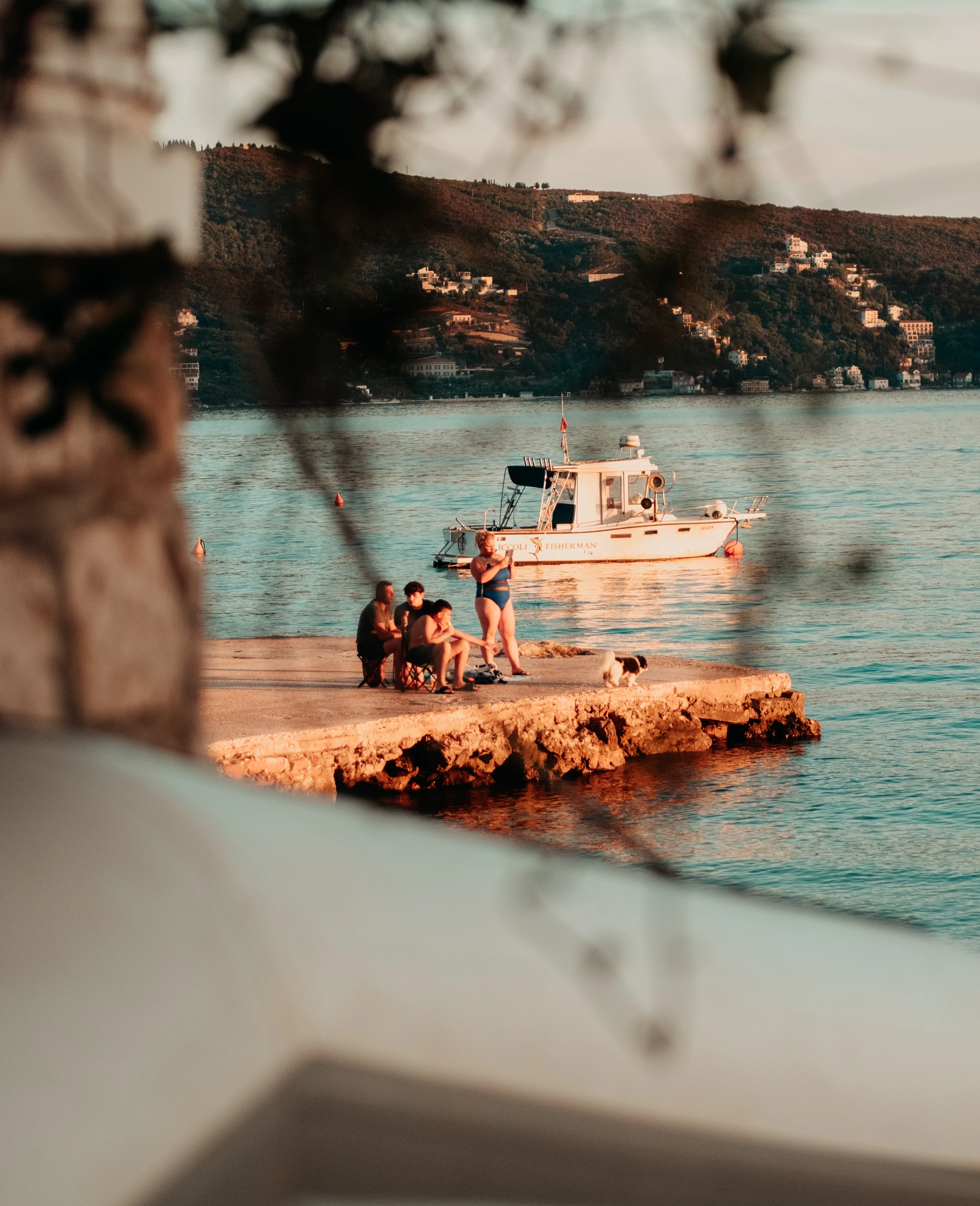 Sunlit waterfront and a small white boat seen through a shaded foreground