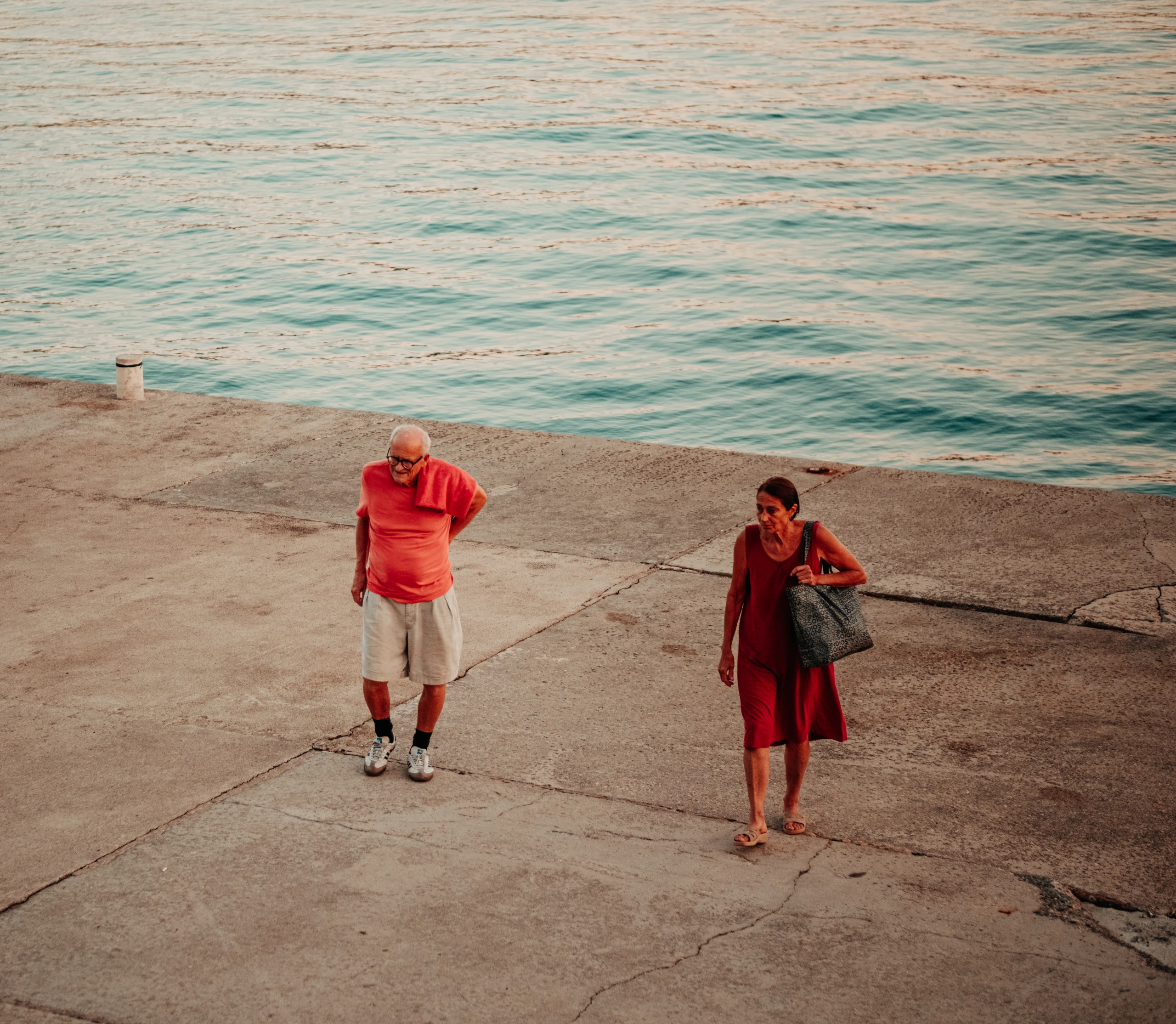 Two people in red clothing standing on a broad concrete waterfront