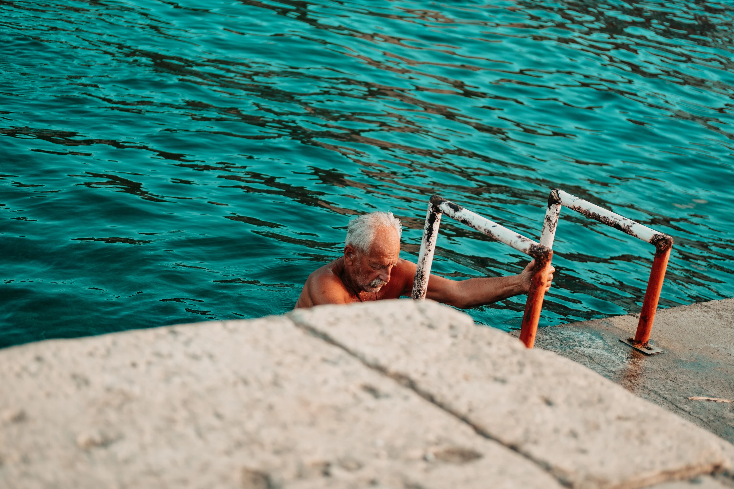 Older man climbing a metal ladder out of turquoise water